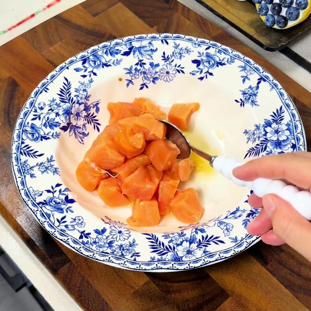 Ein Löffel rührt Lachswürfel in einer blau-weißen Schüssel um, damit sie vollständig von der Marinade bedeckt sind.