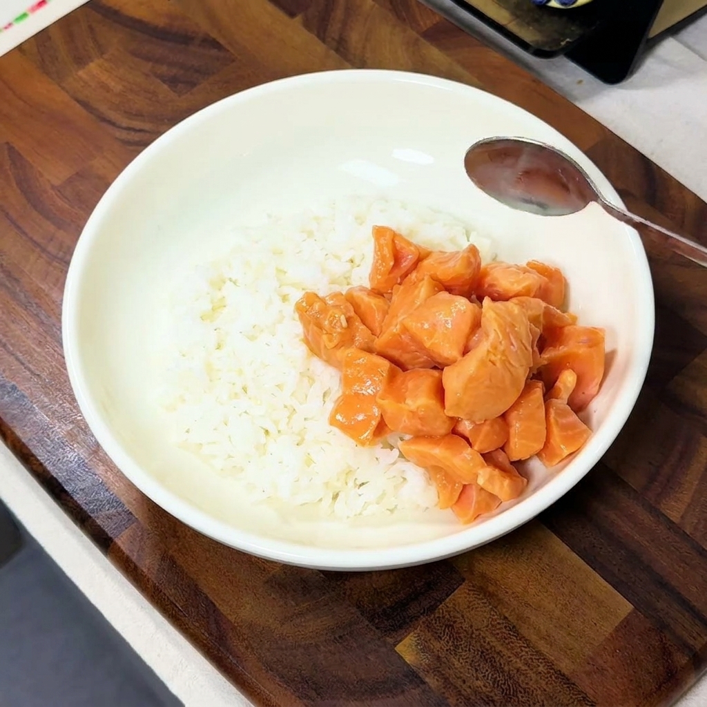 Marinierte Lachswürfel werden auf eine Seite einer Schüssel mit fluffigem weißem Reis gegeben.