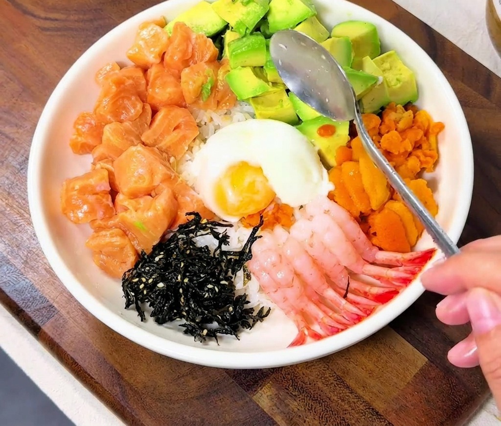 Ein Löffel setzt ein weiches Onsen-Ei in die Mitte der bunt belegten Bowl.