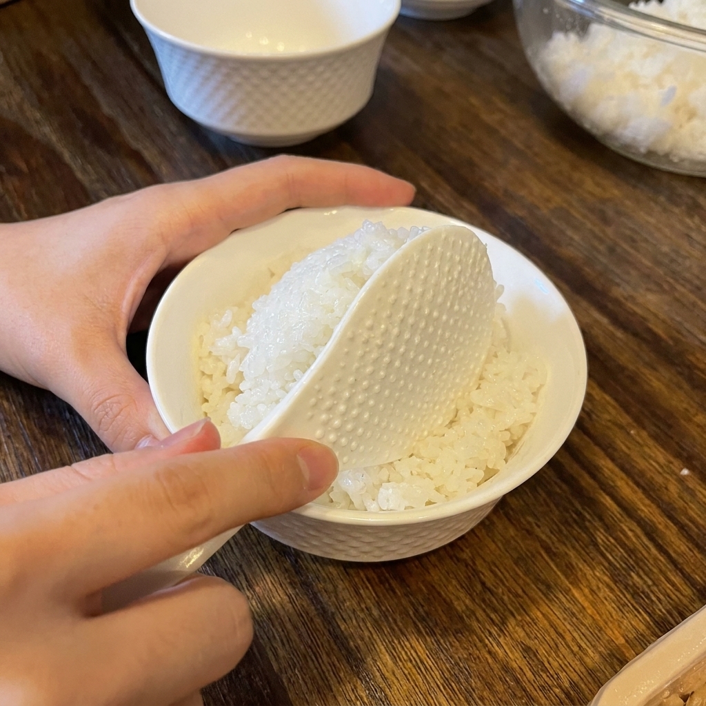 Ein Reislöffel gibt eine Portion gewürzten Reis in eine weiße Keramikschale.