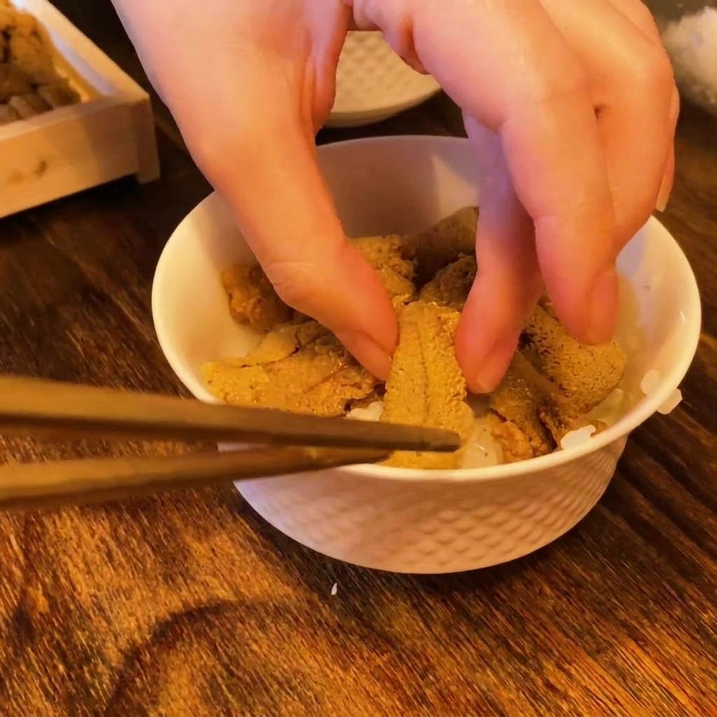 Stäbchen legen leuchtend orangefarbene Seeigel-Stücke auf den weißen Sushi-Reis.