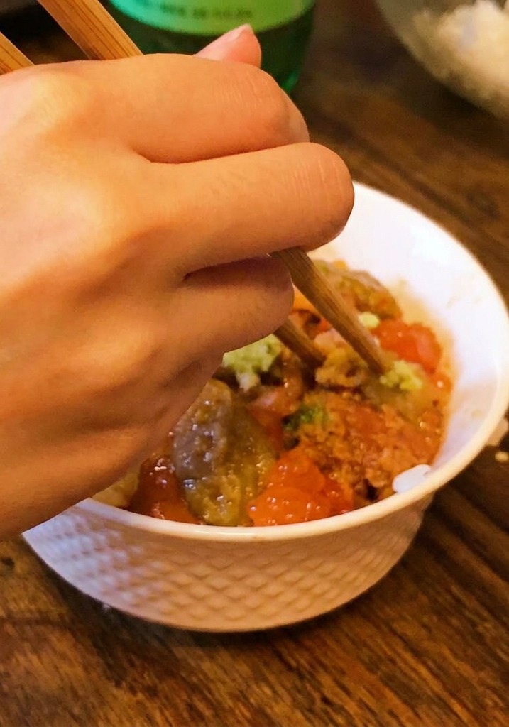 Eine Hand setzt mit Stäbchen einen kleinen Klecks Wasabi in die Mitte der Seafood-Bowl.