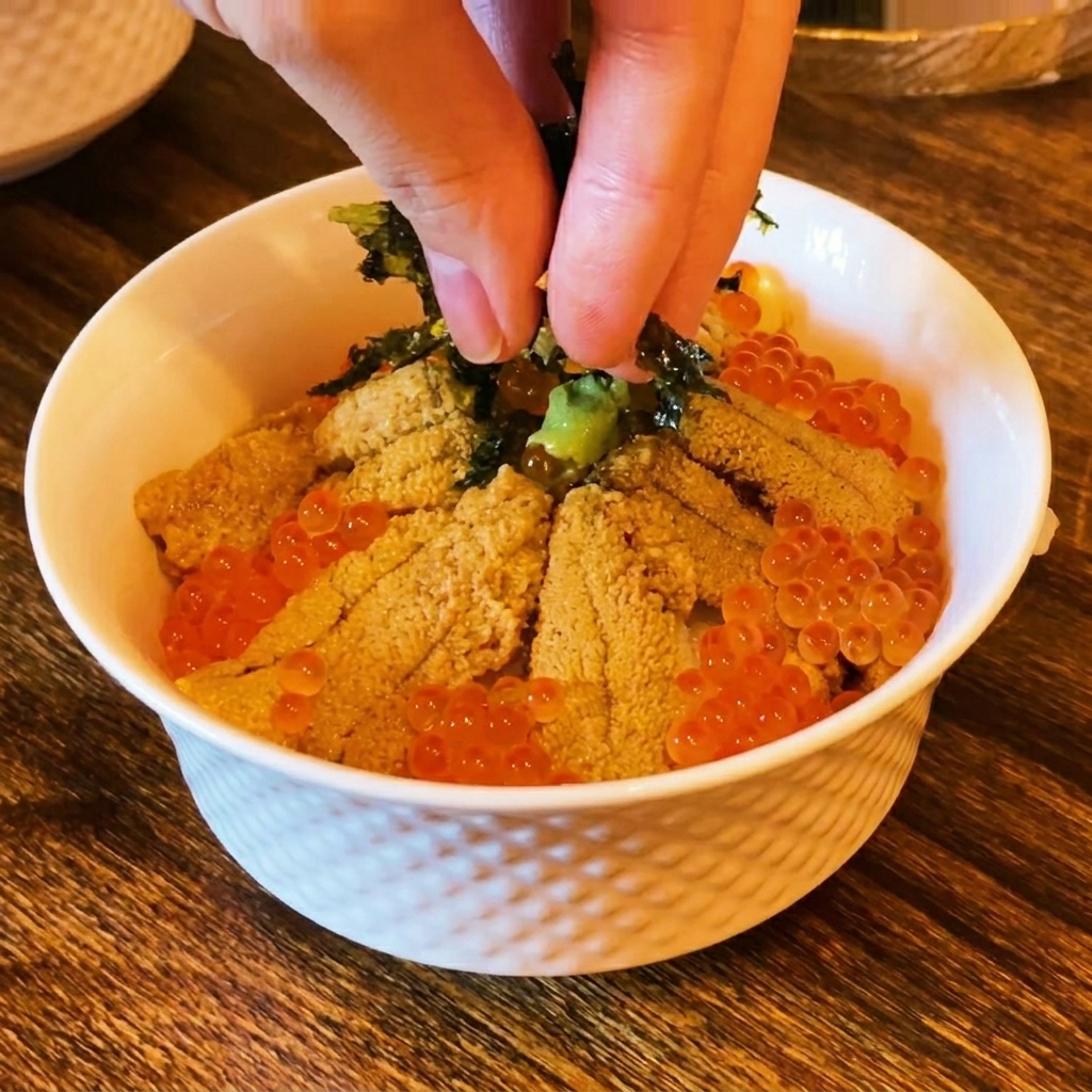 Finger streuen dunkle Nori-Streifen über die Sushi-Bowl mit Seeigel und Lachsrogen.