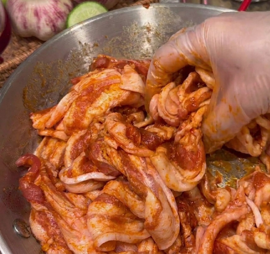 Eine Hand vermengt Schweinebauchscheiben gründlich mit einer dunkelroten Marinade in einer Schüssel.