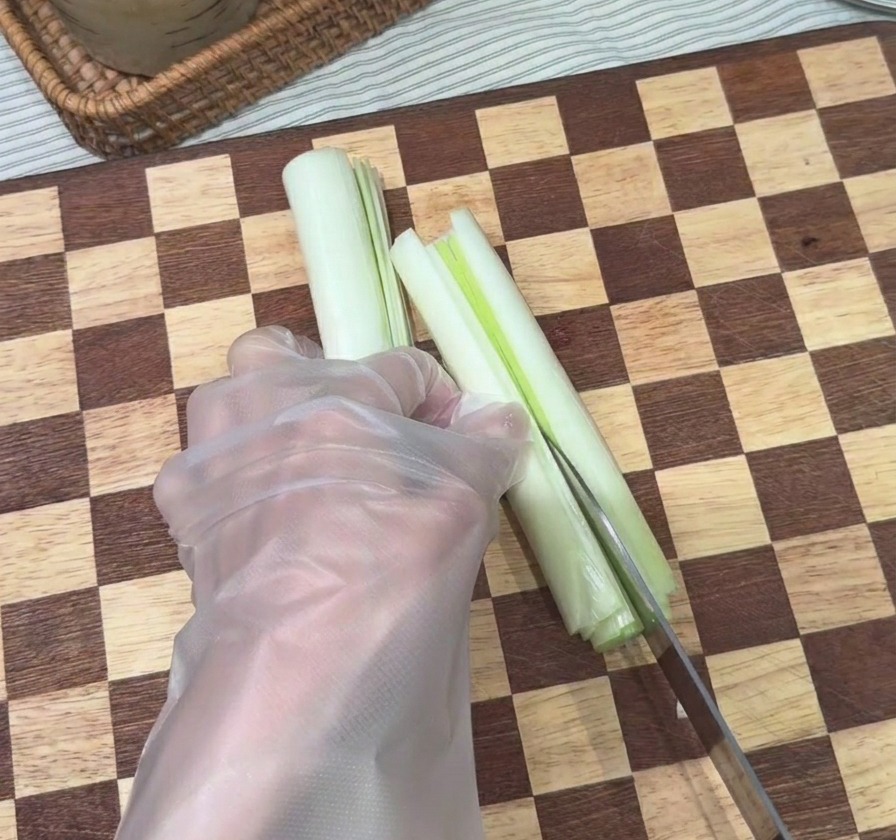 Ein Messer schneidet eine weiße Frühlingszwiebel auf einem Holzbrett in feine, lange Streifen.