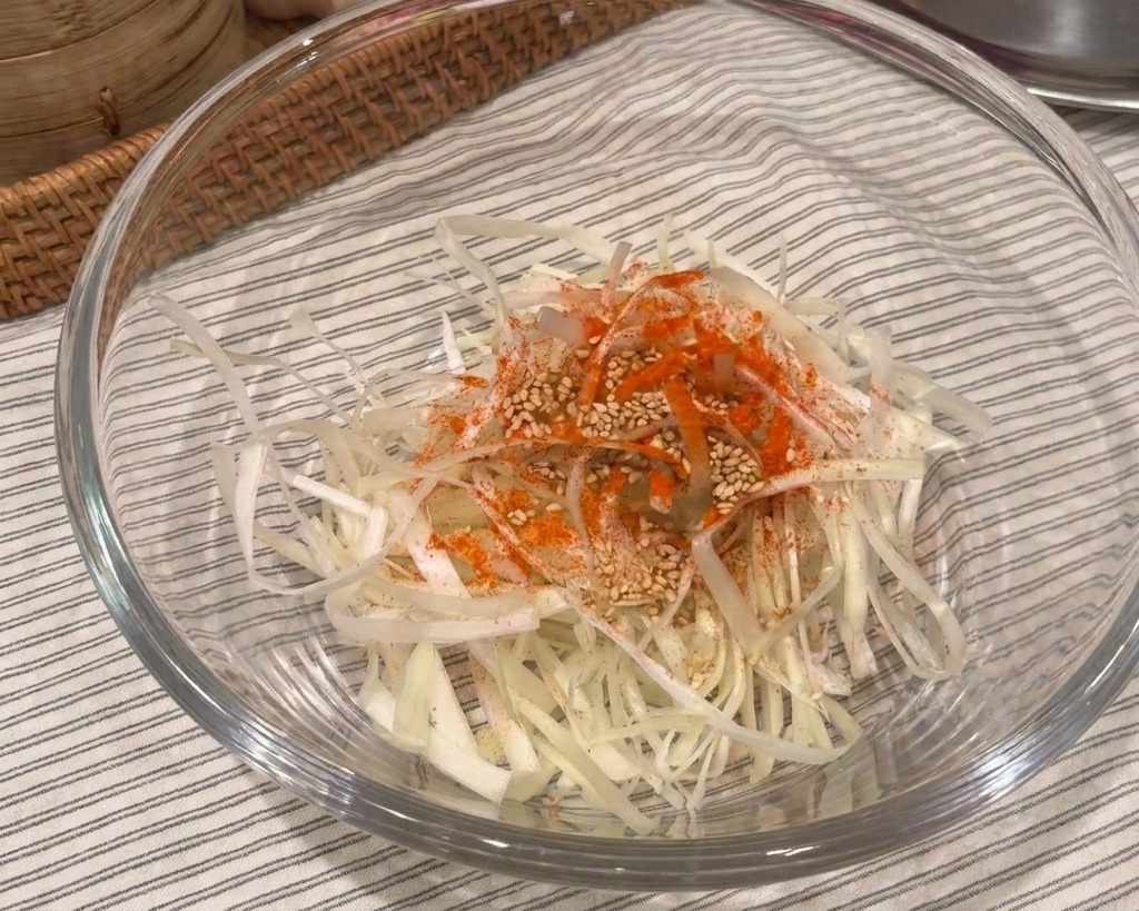 Frühlingszwiebelstreifen in einer Glasschüssel, garniert mit Chilipulver und Sesam.