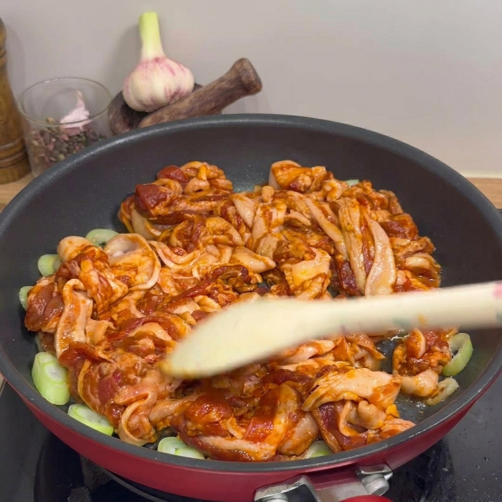 Schweinebauchstreifen werden in einer Pfanne mit einem Holzspatel gewendet, während das Fett ausschmilzt.