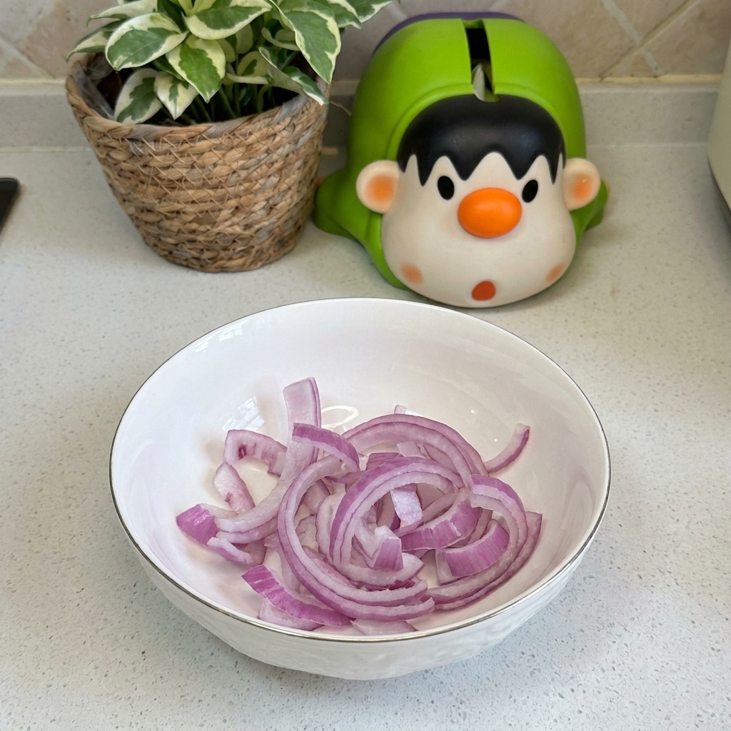 Eine weiße Keramikschüssel auf einer Küchenarbeitsplatte, gefüllt mit frischen, violetten roten Zwiebelringen.