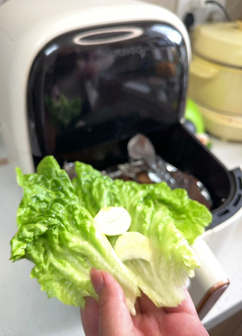 Eine Hand hält ein leuchtend grünes Salatblatt, das mit zwei dünnen Scheiben weißem Knoblauch und roten Zwiebelringen belegt ist.