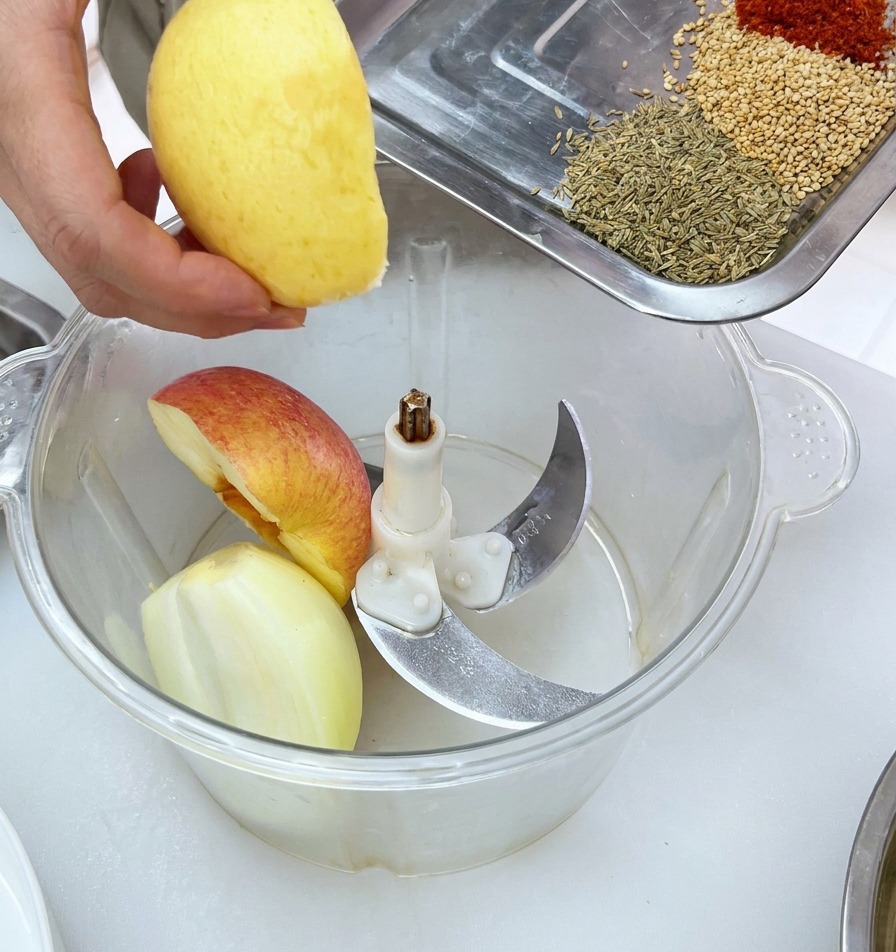Frische Obststücke werden zusammen mit Gewürzen in den Behälter eines Mixers gegeben.