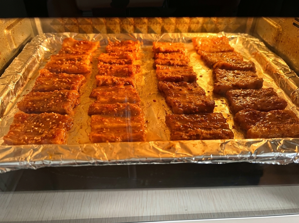 Schweinebauchscheiben rösten auf einem Blech im beleuchteten Backofen.