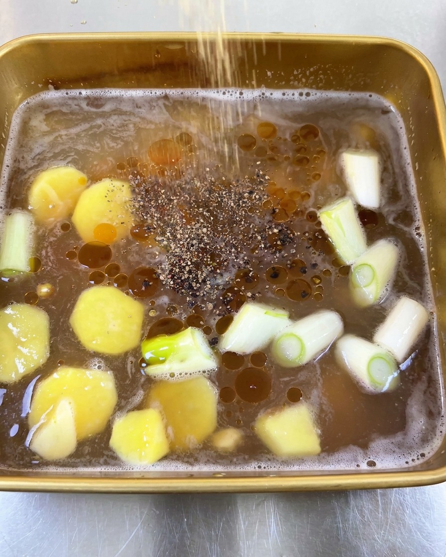 Schwarzer Pfeffer wird über die flüssige Marinade mit Öltröpfchen, Ingwer und Frühlingszwiebeln gestreut.