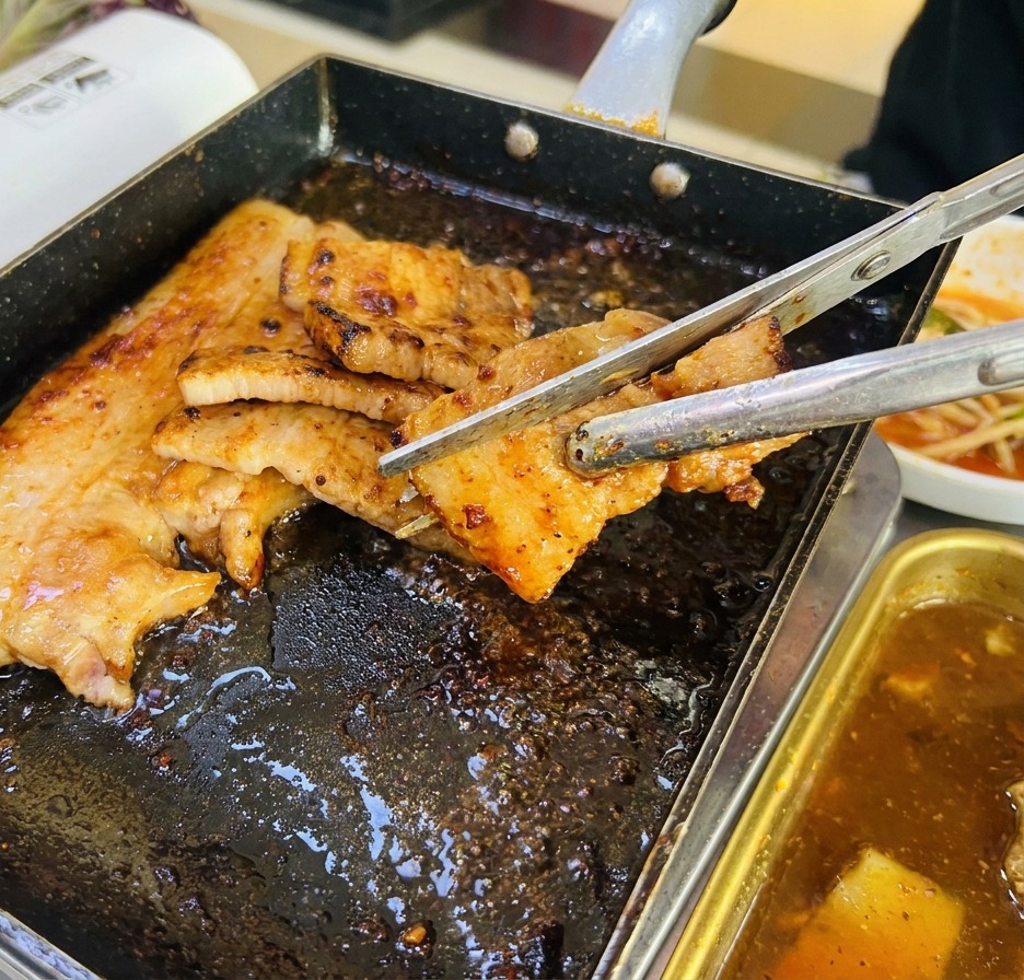 Nahaufnahme von Schweinebauchscheiben, die mit einer Küchenschere direkt in der Grillpfanne in Stücke geschnitten werden.