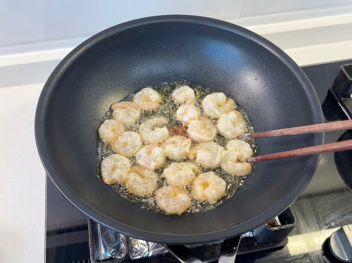 Garnelen werden mit Holzstäbchen in einem schwarzen Wok mit heißem Öl gebraten.
