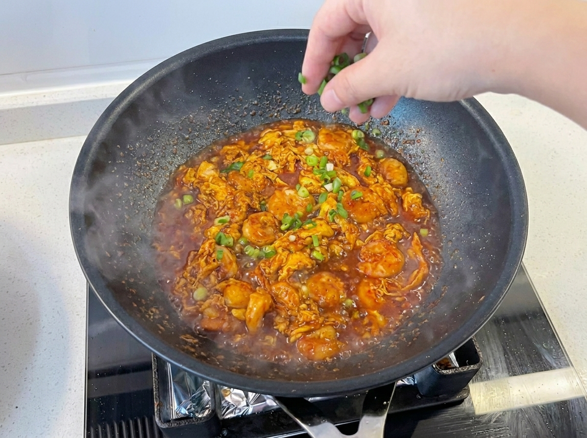 Frisch gehackte Frühlingszwiebeln werden über das fertige Gericht in der Pfanne gestreut.