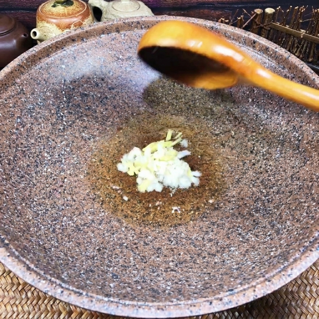 Gehackter Knoblauch und Ingwer brutzeln in etwas Öl am Boden eines dunklen Woks.