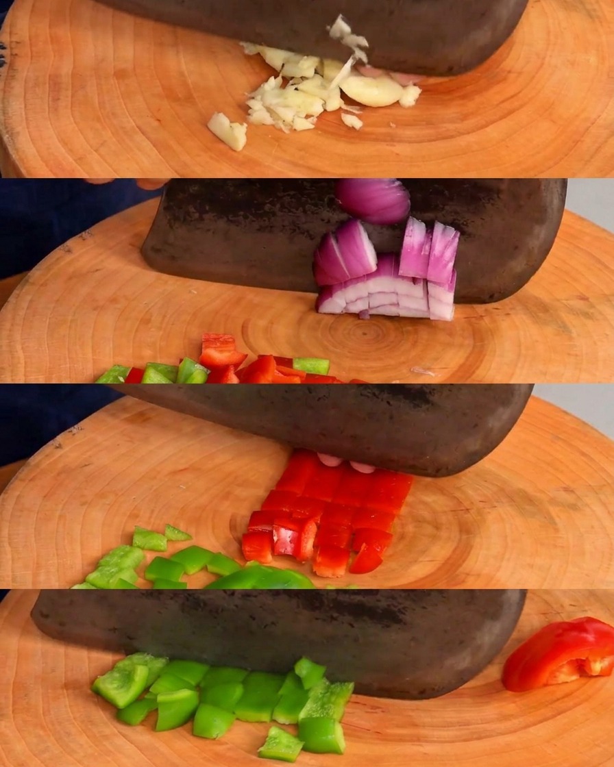 Gehackter Knoblauch sowie gewürfelte Paprika und Zwiebeln auf einem runden Holzschneidebrett.