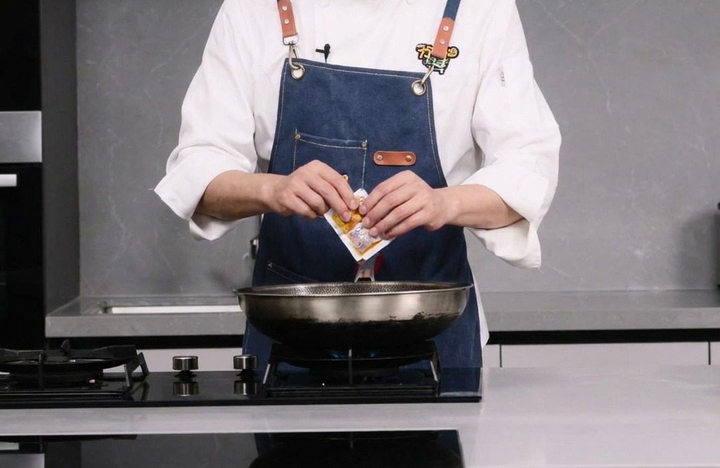 Eine Person öffnet eine Packung mit scharfer Hot-Pot-Basis über einem Wok.