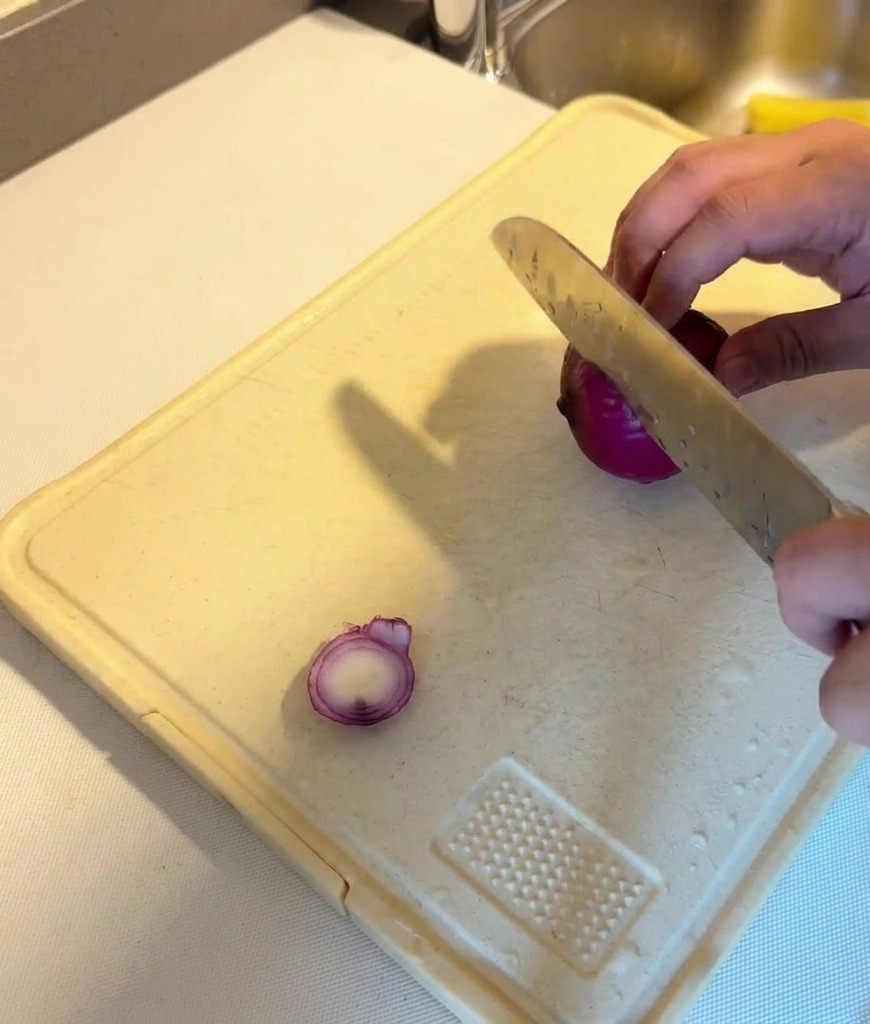 Eine Person schneidet eine rote Zwiebel mit einem scharfen Messer in feine Streifen.