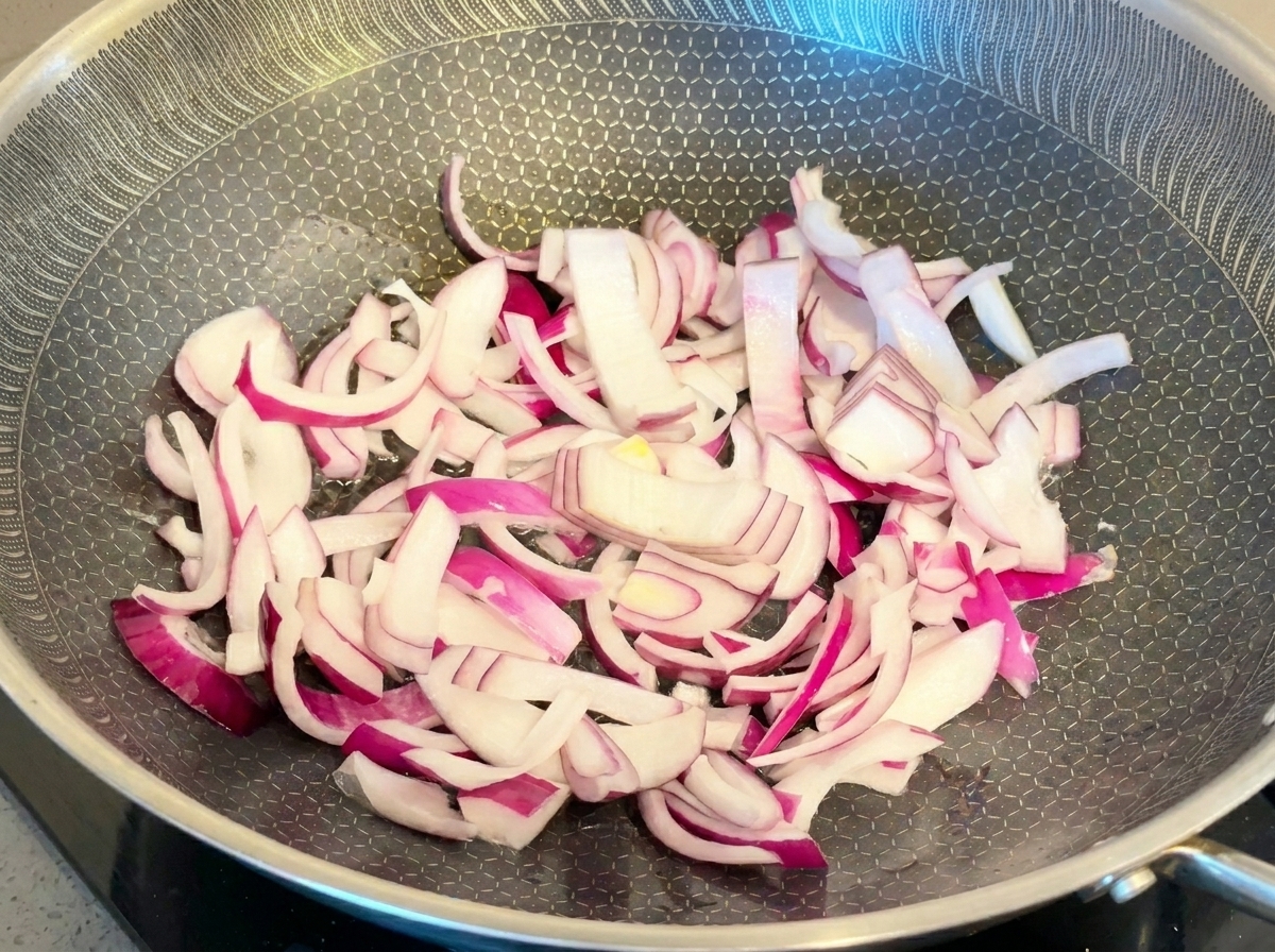 Leuchtend rote Zwiebelstreifen werden in einer Metallpfanne angebraten.