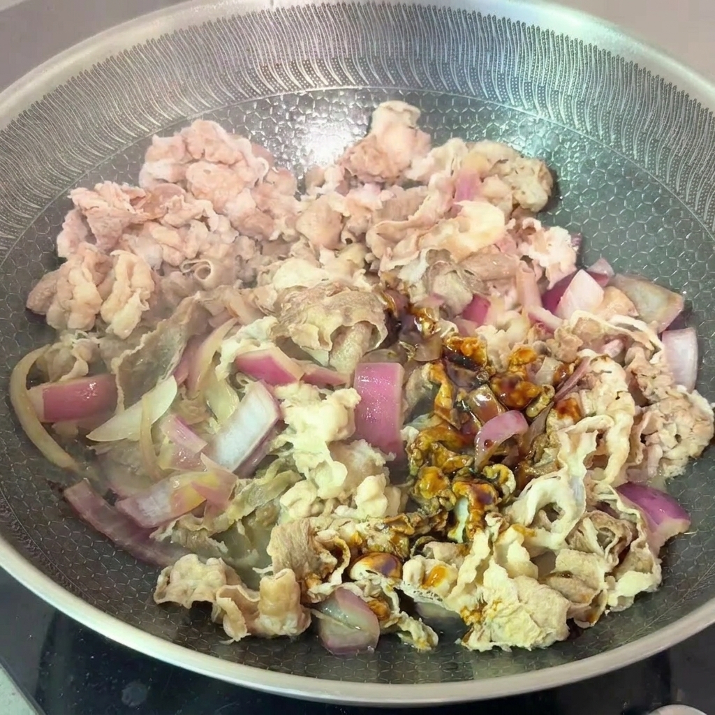 Blanchierte Rindfleischstreifen und Zwiebeln werden mit einer dunklen Sojasauce in der Pfanne geschwenkt.