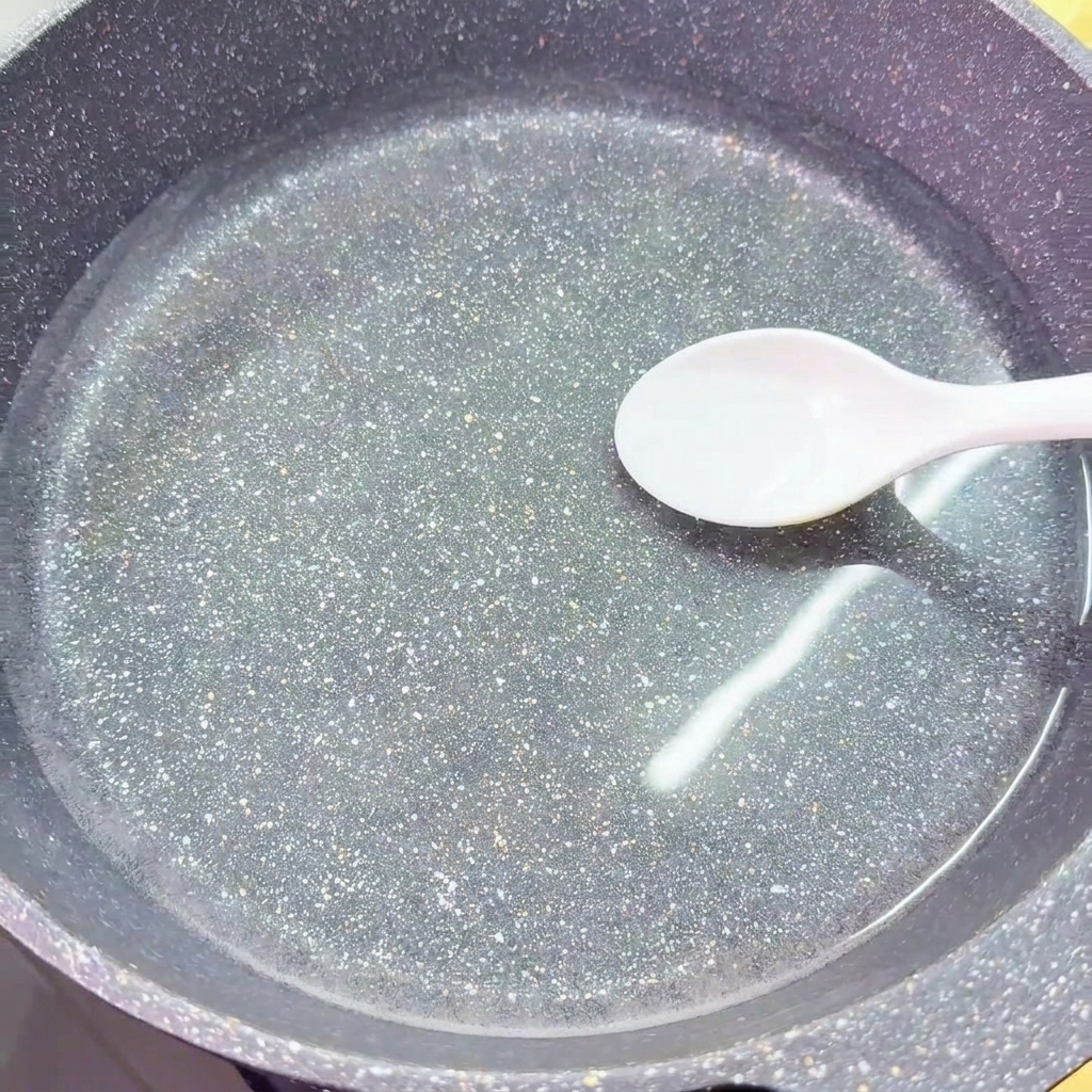 Ein weißer Löffel gibt eine Portion Salz in einen Wok mit klarem, kaltem Wasser.