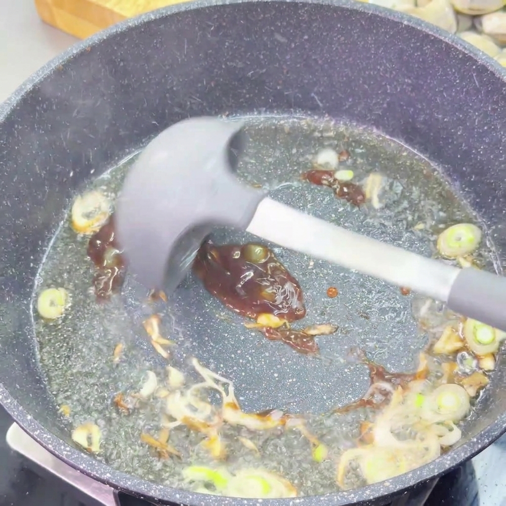 Dunkle, dicke Austernsauce wird mit einem Silikonspatel unter die angebratenen Frühlingszwiebeln gerührt.