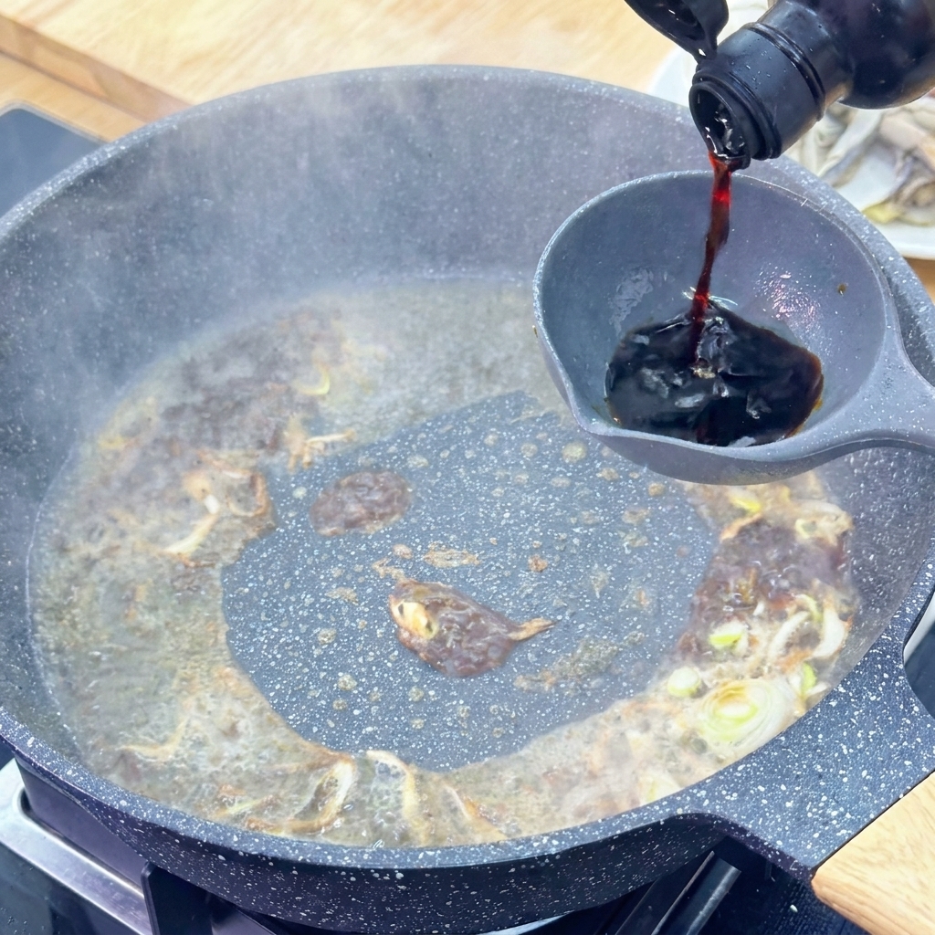 Helle Sojasauce wird aus einer dunklen Glasflasche in eine Kelle über der köchelnden Sauce gegossen.