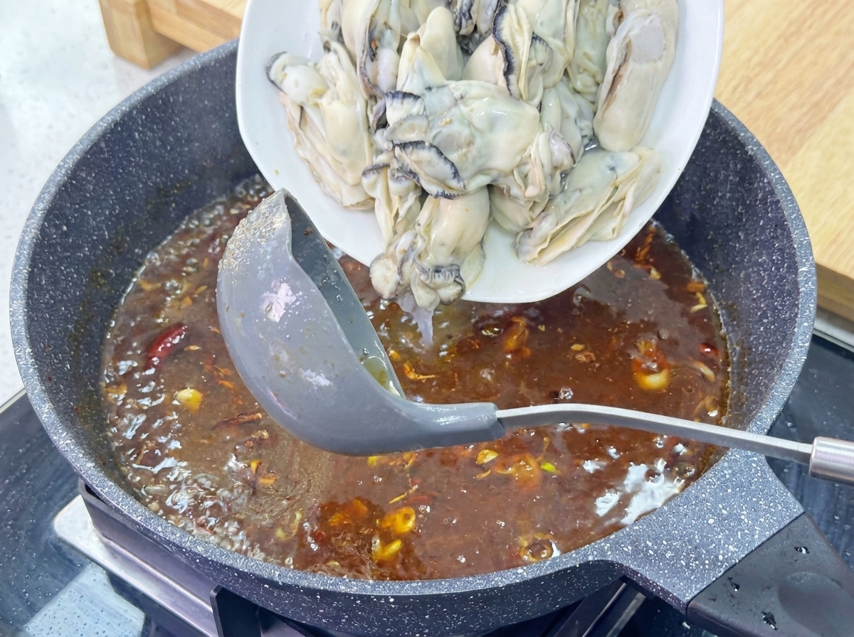 Ein Teller mit großen, prallen Austern wird in eine köchelnde braune Sauce geschoben.