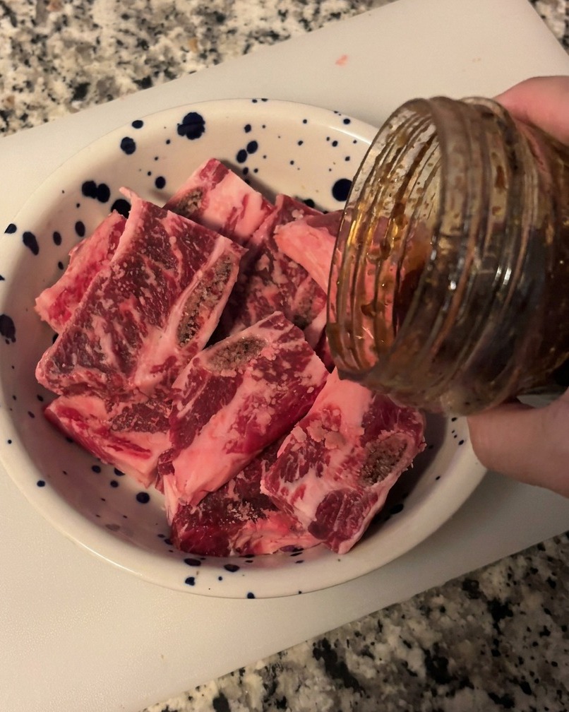 Dunkle, glänzende Galbi-Sauce wird aus einem Glas über die Fleischstücke in eine Schüssel gegossen.