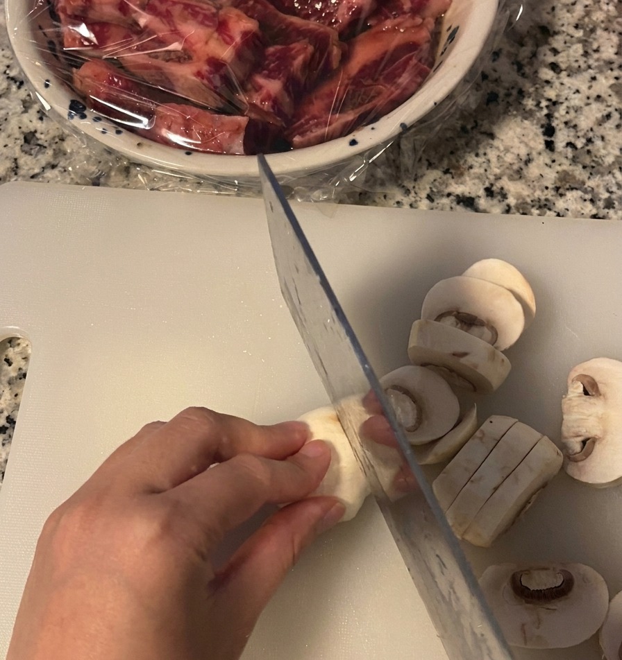 Eine Hand schneidet einen weißen Champignon auf einem Brett in dicke Scheiben.