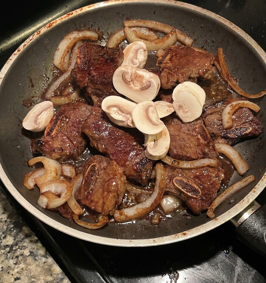 Pilze werden mit Fleisch und Zwiebeln in einer dunklen Pfanne pfannengerührt.