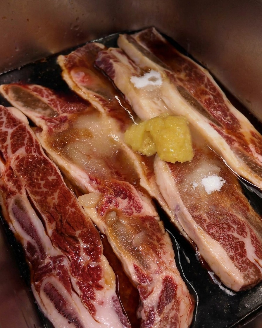 Ein Häufchen gehackter Knoblauch liegt auf dem marmorierten Fleisch in der Marinade.