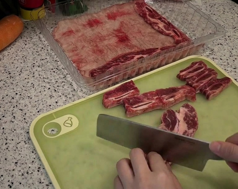 Rinderkurzrippen werden mit einem Messer auf einem grünen Brett in gleichmäßige Stücke geschnitten.