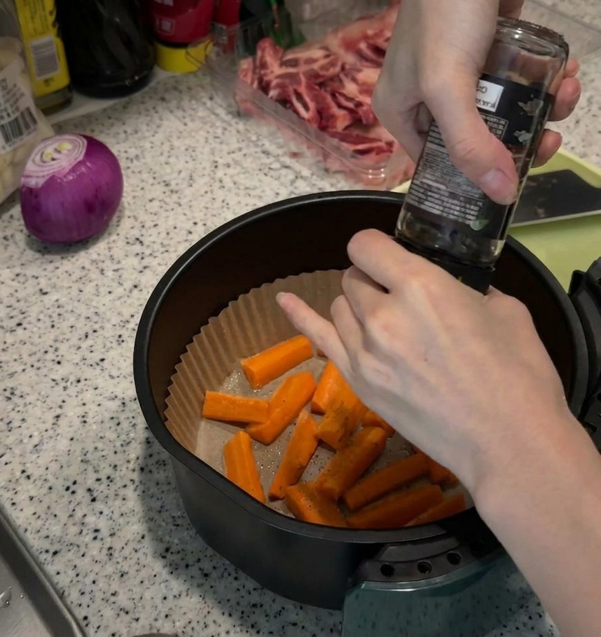 Karottenstifte in einer Heißluftfritteuse werden mit frisch gemahlenem Pfeffer gewürzt.