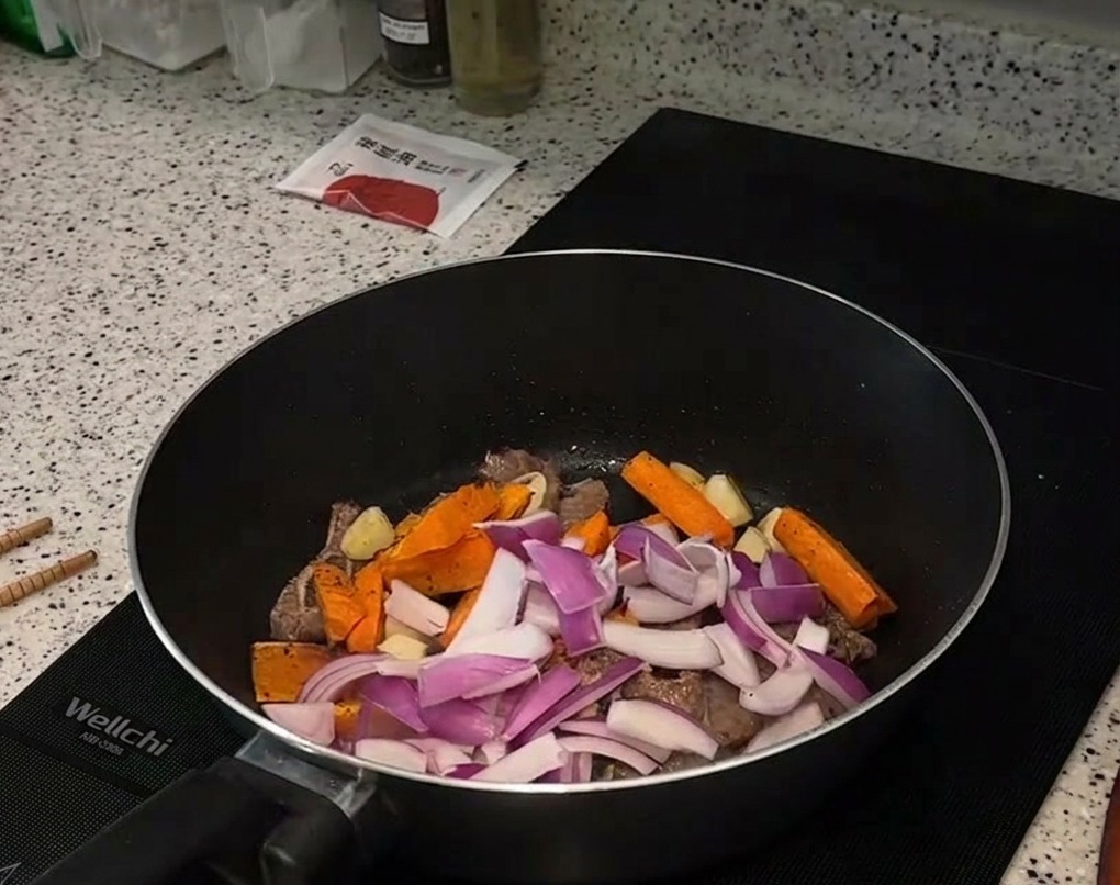 Rote Zwiebeln und geröstete Karotten werden zum Fleisch in die Pfanne gegeben.
