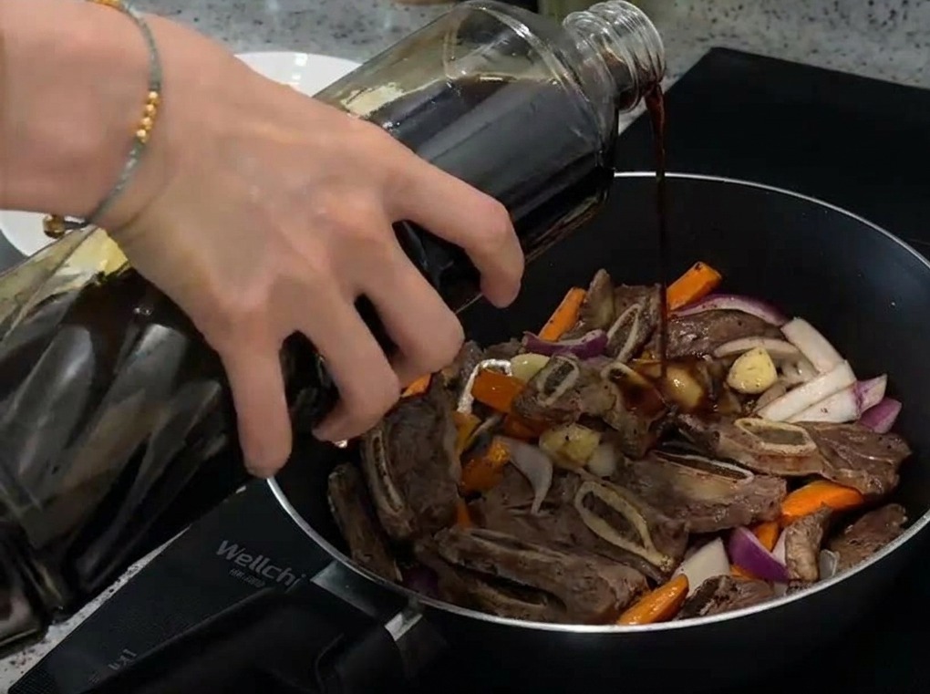 Helle Sojasauce wird über die Fleisch-Gemüse-Mischung in der Pfanne gegossen.