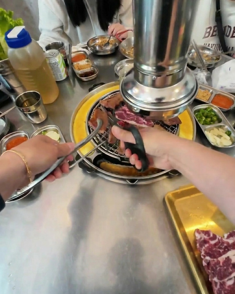 Nahaufnahme einer Küchenschere, die gegrilltes Rindfleisch über den Kohlen in kleine Quadrate schneidet.