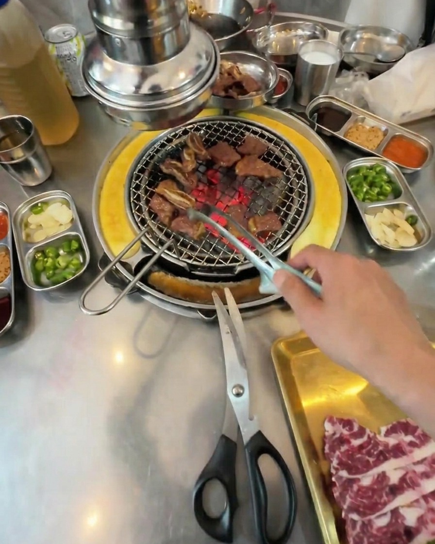 Kleine Würfel aus fertig gegrilltem Rindfleisch werden mit einer Zange auf dem Grillrost gewendet.