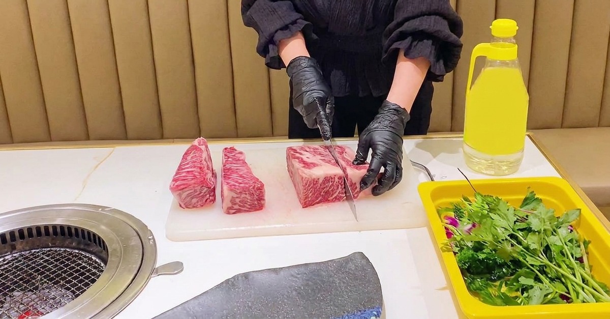 Eine Person mit schwarzen Handschuhen schneidet eine große, marmorierte rohe Rinderkurzrippe in gleichmäßige rechteckige Abschnitte.
