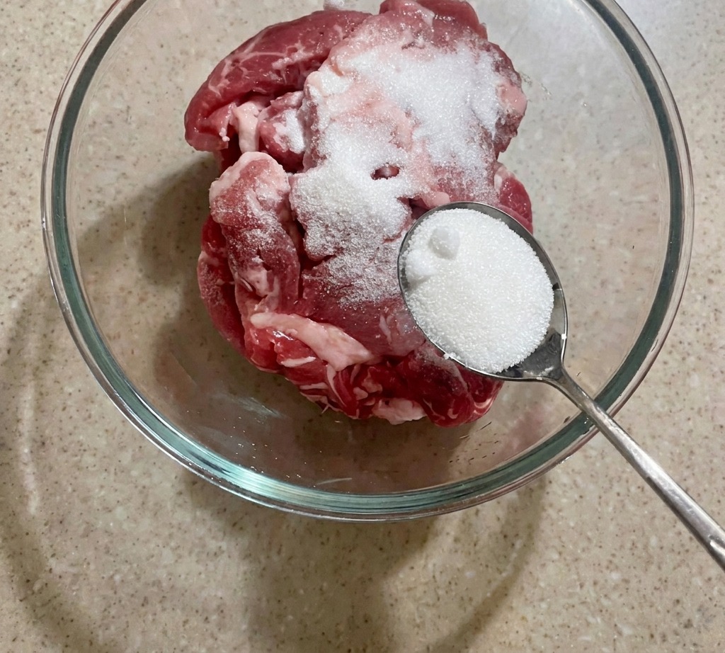 In Streifen geschnittenes Schweinefleisch wird in einer Schüssel mit einer Portion Zucker bestreut.