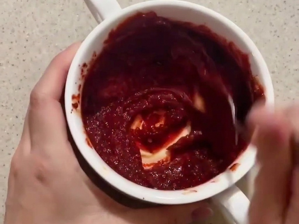 Eine tiefrote, dickflüssige Sauce wird in einer kleinen weißen Schüssel mit einem Löffel glatt gerührt.