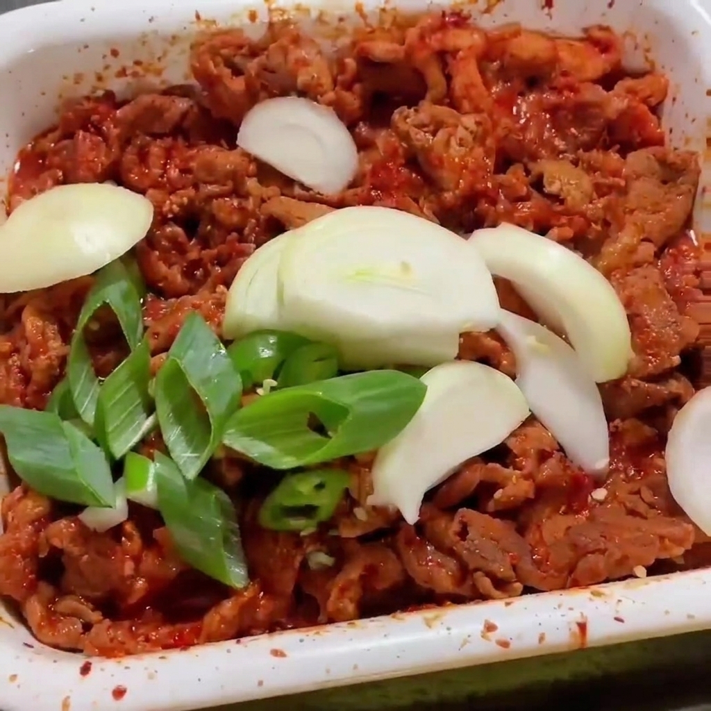 Frisch geschnittene Zwiebeln und Frühlingszwiebeln liegen auf dem scharf gewürzten Fleisch in der Pfanne.