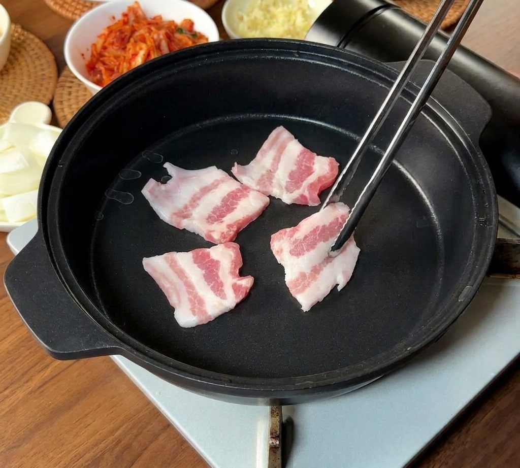Dünne Streifen von rohem, marmoriertem Schweinebauch werden mit Metallstäbchen in eine schwarze Pfanne gelegt.