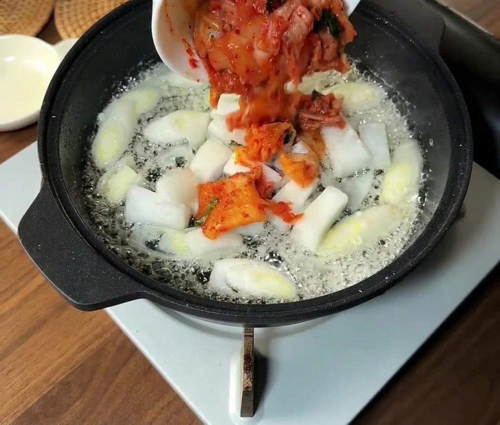 Gehacktes Kimchi und Zwiebelscheiben werden zu den gedünsteten Frühlingszwiebeln in die Pfanne gegeben.