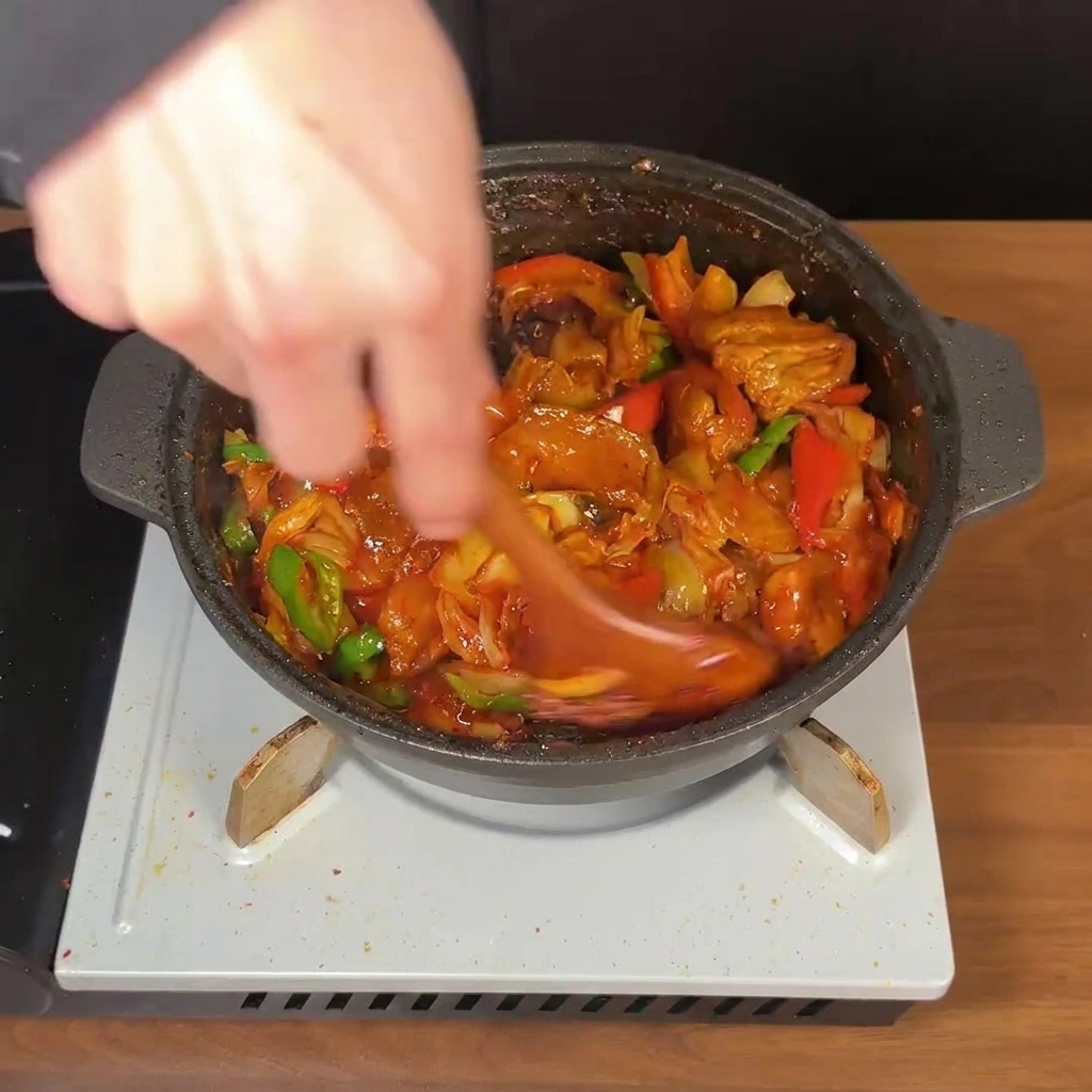 Ein Holzlöffel rührt kräftig in einer Pfanne mit scharfem Schweinebauch, Kimchi und Paprika in dicker roter Sauce.