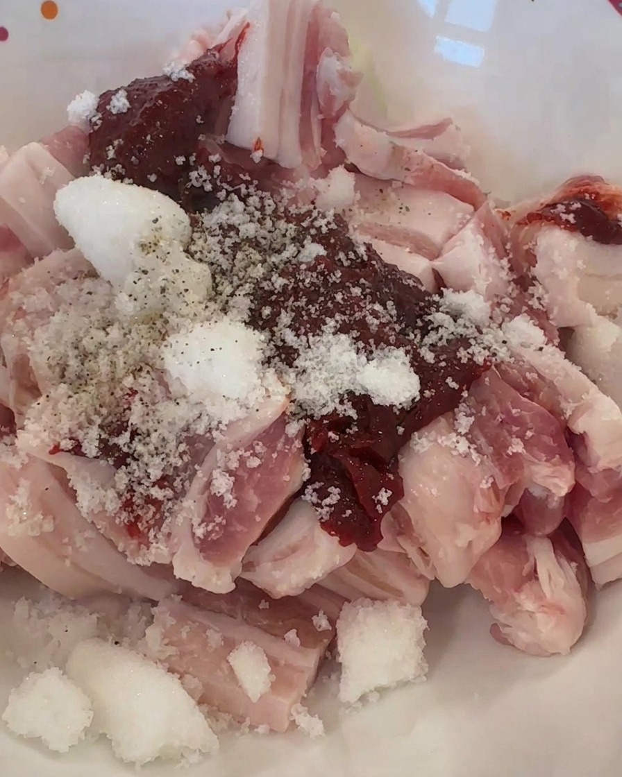 Rohe Schweinefleischstreifen in einer Schüssel mit roter Chilipaste, Zucker und schwarzem Pfeffer.