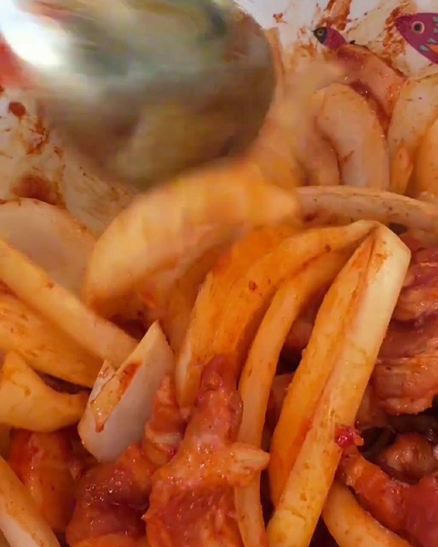 Große weiße Zwiebelscheiben werden unter das scharf marinierte Schweinefleisch gemischt.
