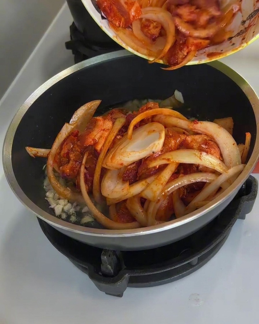 Scharfes Schweinefleisch und Zwiebeln garen in der Pfanne, Dampf steigt auf und die Sauce blubbert.