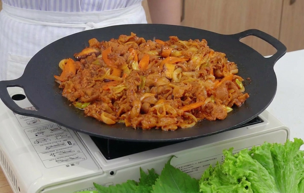 Nahaufnahme von geröstetem Sesam, der über eine dampfende Pfanne mit scharfem Schweinefleisch und Gemüse gestreut wird.